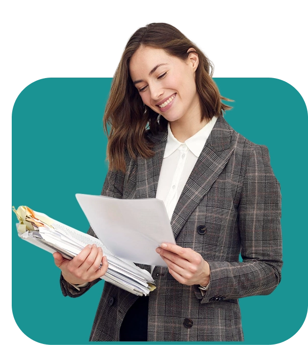 Un homme souriant, vêtu d'une casquette bleue et d'une salopette, tient un bloc-notes et un stylo, debout face à droite sur un fond blanc uni, dégageant une attitude amicale.