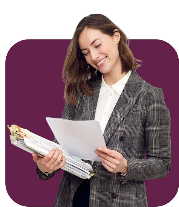 Un homme souriant, vêtu d'une casquette bleue et d'une salopette, tient un bloc-notes et un stylo, debout face à droite sur un fond blanc uni, dégageant une attitude amicale.